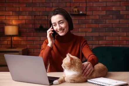 una mujer hablando por el móvil mirando el portátil mientras acaricia a un gato